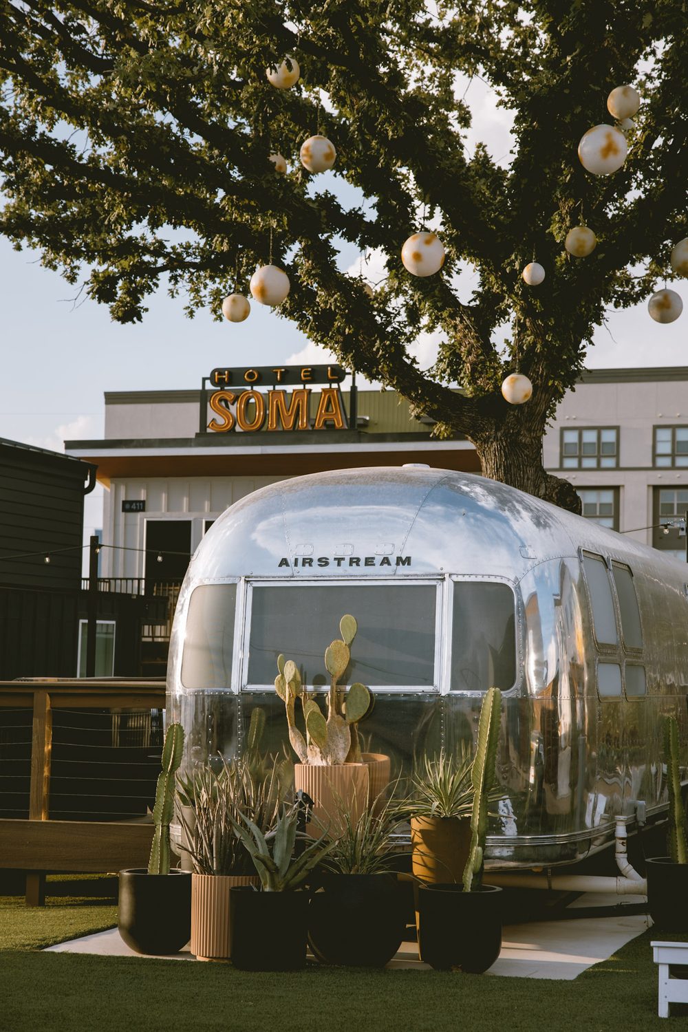Silver Airstream suite with potted cactus under the courtyard oak, with the Hotel SOMA sign behind it in South Main Village