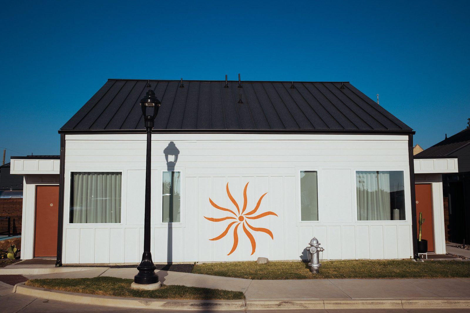 Hotel SOMA casita with the orange sunburst mark and a vintage street lamp on a quiet street in South Main Village, Fort Worth's Near Southside